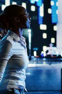 Smiling african american woman wandering around city boulevards during nighttime, pointing at interesting billboards on skyscrapers. Businesswoman strolling around streets illuminated by lamps